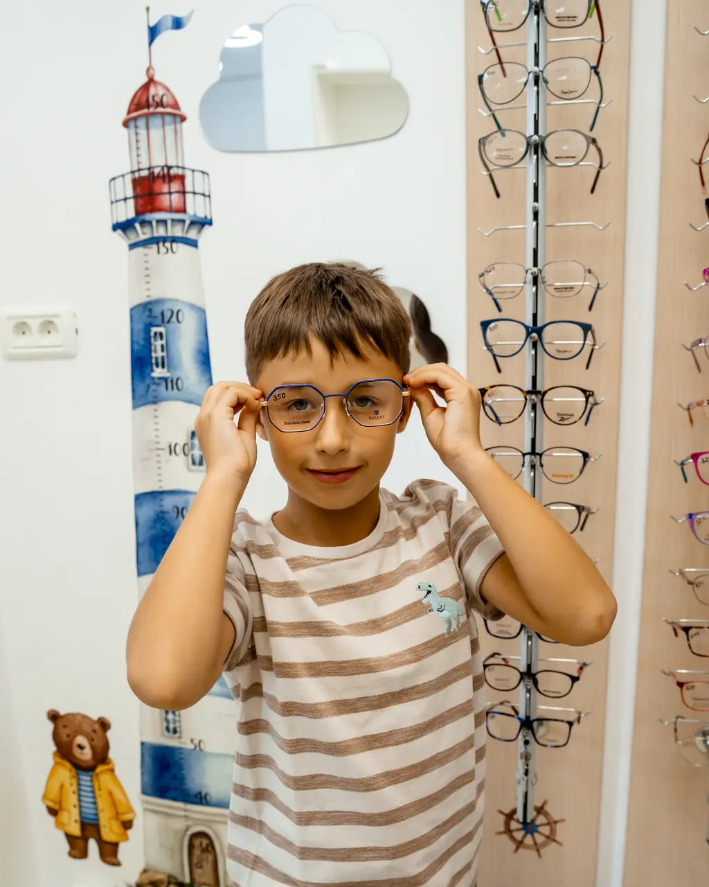 Băiețel care își potrivește ochelarii noi în colțul pentru copii al magazinului